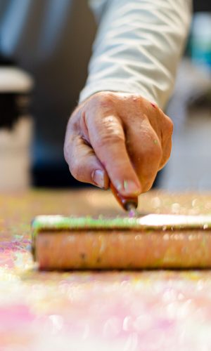 Hier sieht man die Hand von Harry Bauer an einem Pinselroller beim Erstellen eines Kunstwerks in seinem Atelier in Deggendorf.